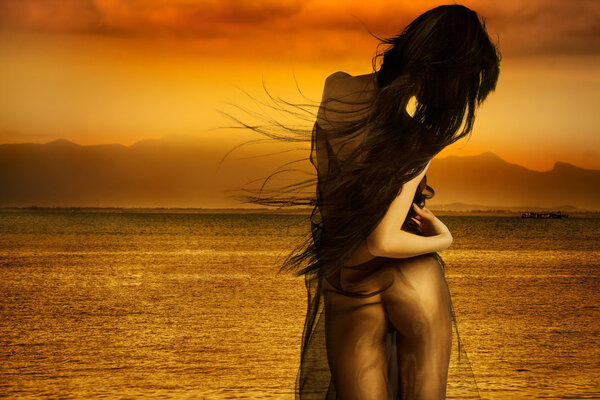 Sexy model with hair blowing in wind and sunset ocean in background