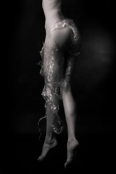 stock image Naked girl, covered with plastic film on a dark background.