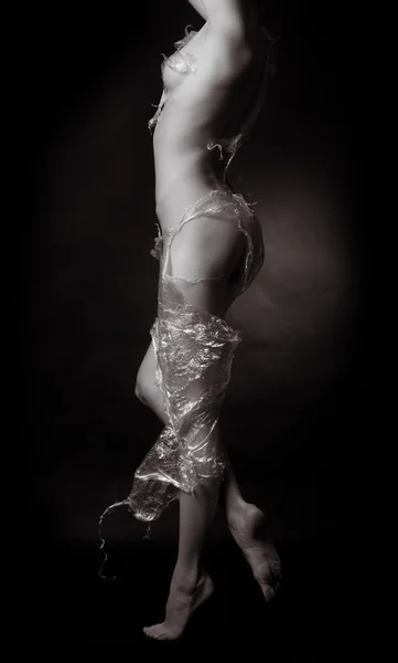 stock image Naked girl, covered with plastic film on a dark background.